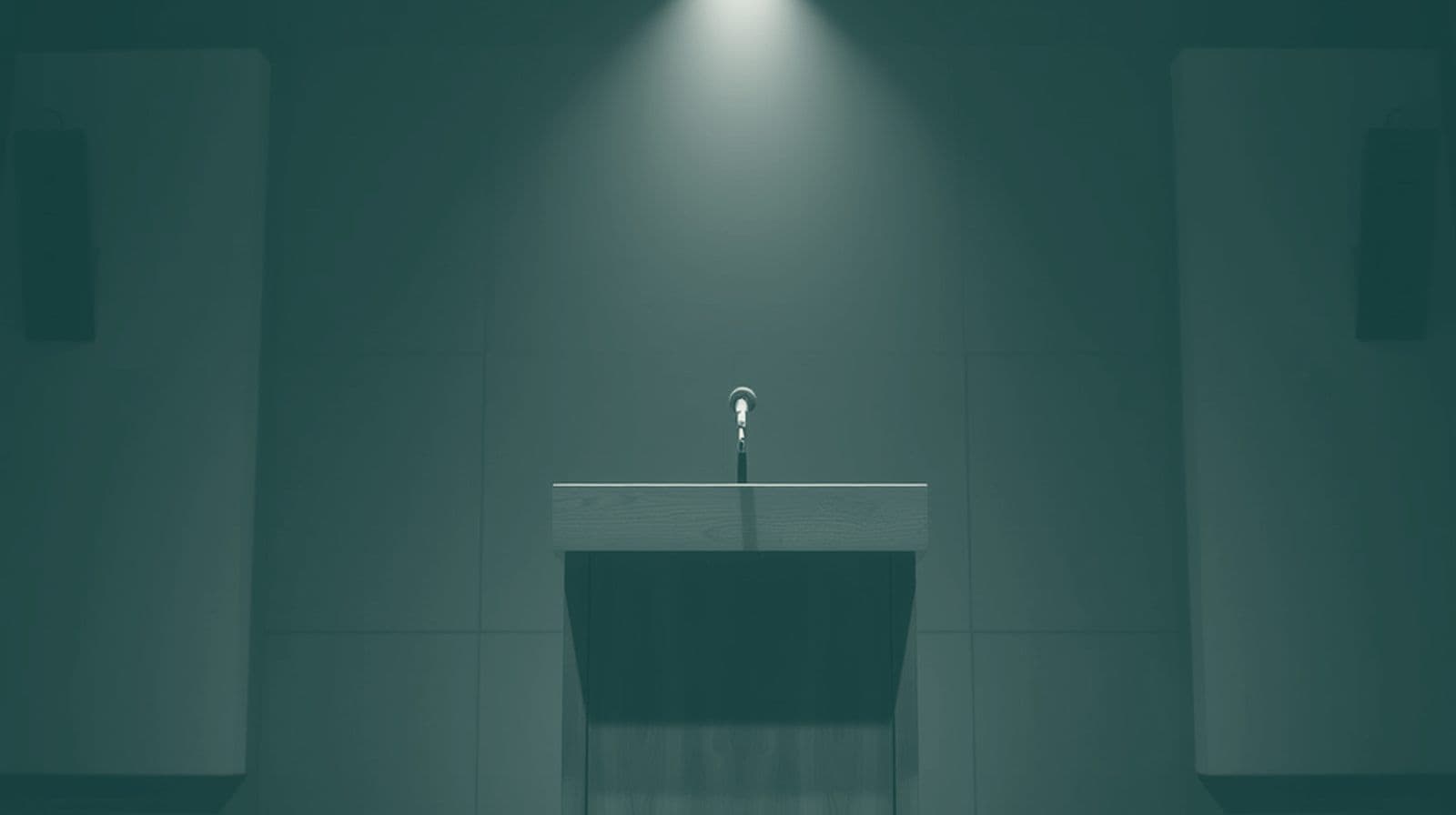 An empty lectern with a small microphone on a stage under cool overhead spotlights.