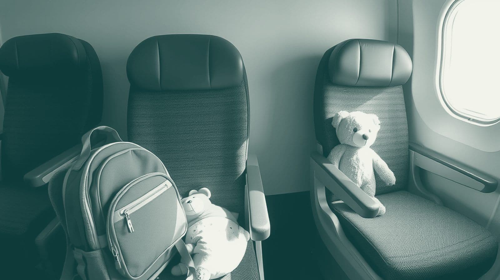 Two empty airline seats side by side, with a child's backpack and a teddy bear on one, in soft window light