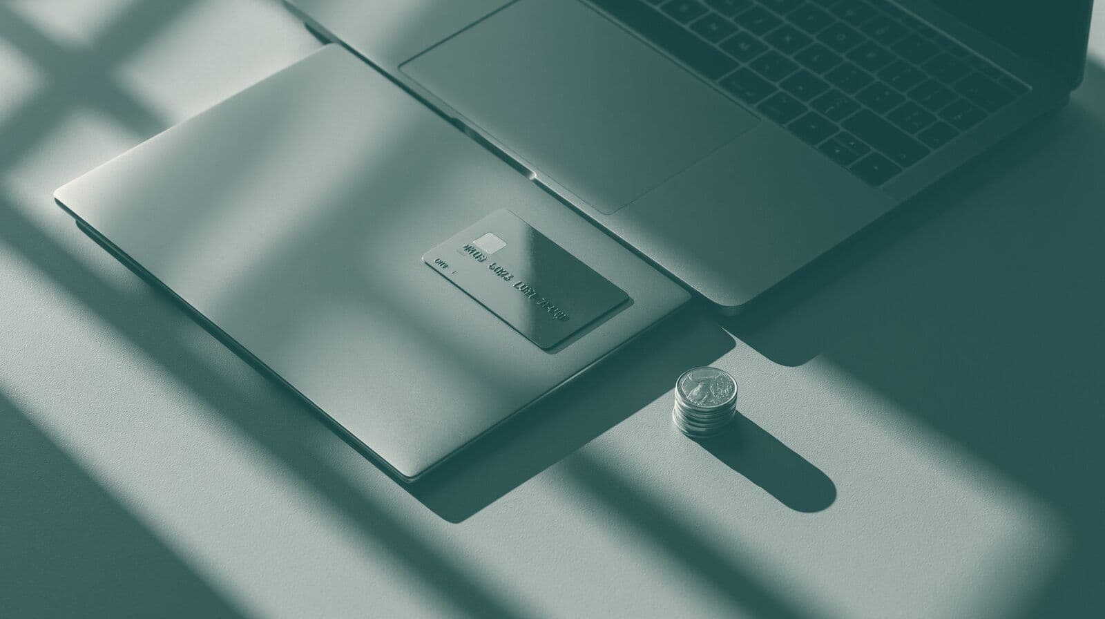 A bank card resting on a closed laptop next to a small stack of coins.